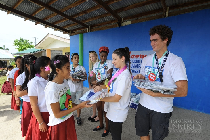 Limkokwing international student ambassadors giving out school supplies to the students of Libaong National High School